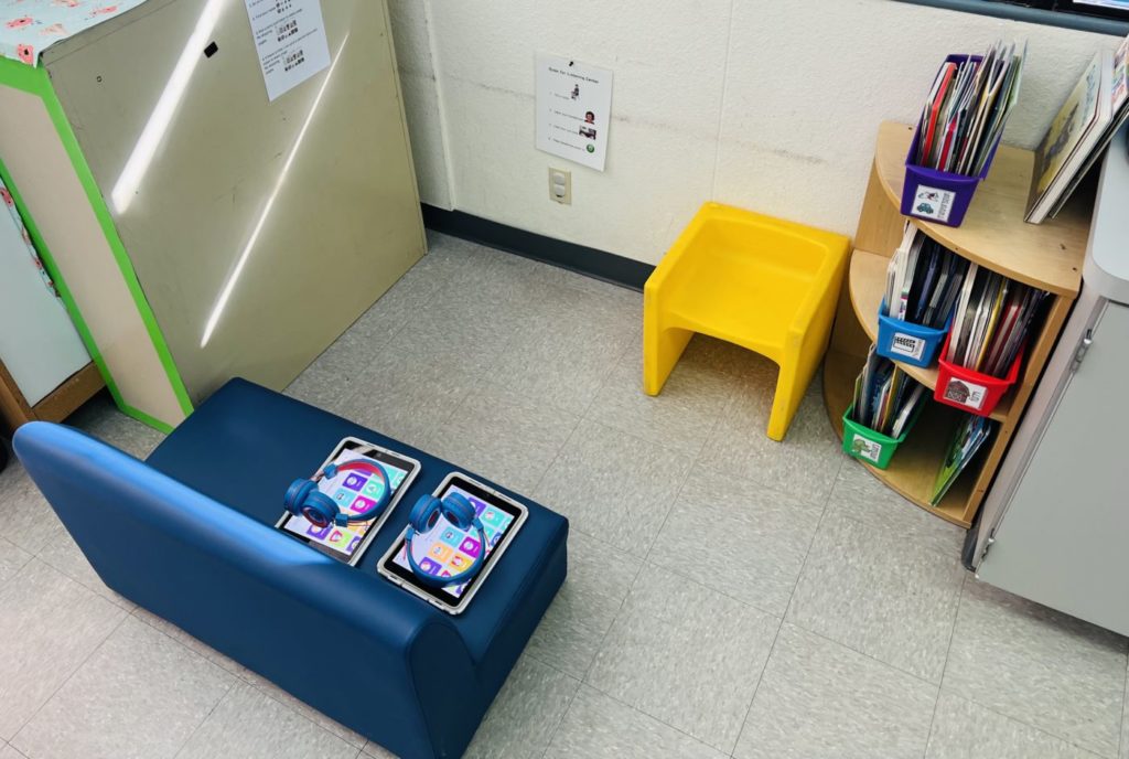 This photo shows my book center, an easy setup independent center. In the photo, you see a small couch with two iPads, a shelf with some books on it, and a yellow child's chair.